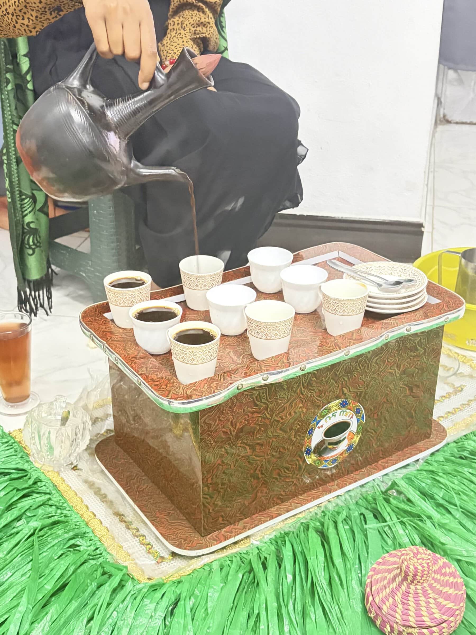 Coffee is poured from a metal pot into small cups arranged on a decorated serving tray during an Ethiopian coffee ceremony.