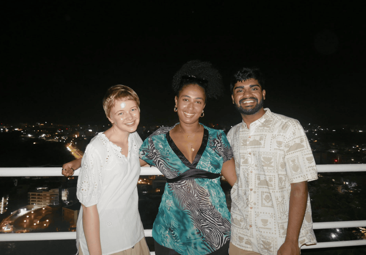 Susannah Owen ’28, Anjali Sankale ’28 and Suhan Asaigoli ’27 stand together at Phare des Mamelles, a lighthouse-turned-restaurant overlooking Dakar, Senegal. At night, city lights and a stretch of water are visible behind them.