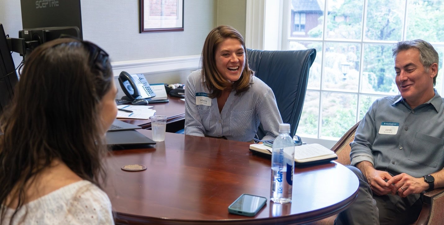 Three people talking around an office desk, smiling.